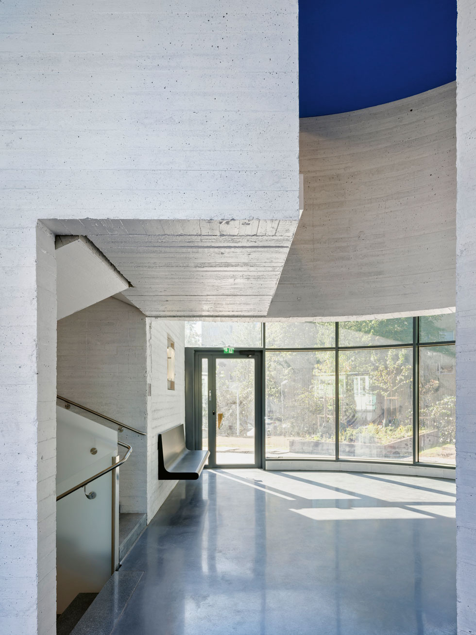 Valoisissa aulatiloissa on Meanderiin suunniteltuja penkkejä ja valaisimia. Paikallavaletut lautamuottipintaiset betoniseinät on maalattu valkoiseksi. Kuva: Anders Portman